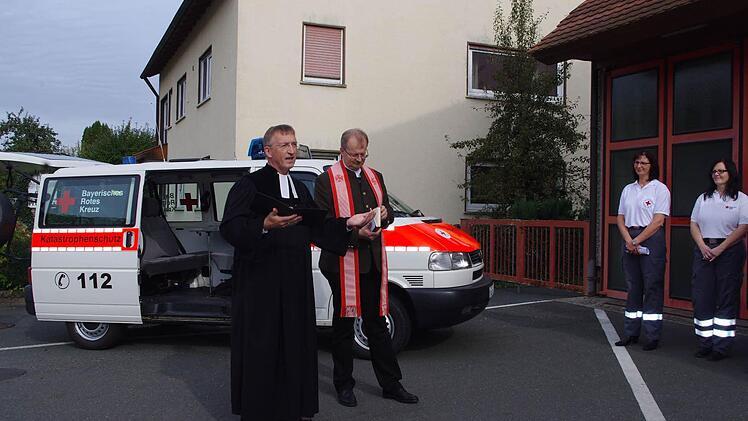 Pfarrer Gerald Munzert und Regionaldekan Thomas Teuchgräber segnen den Mannschaftstransportwagens vor. Mit im Bild sind (ab dritte von links) Bereitschaftsleiterin Thea Biesenecker und ihre Stellvertreterin Marina Zwingmann. Foto: Heike Schülein
