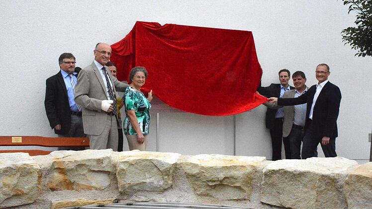 Eine Schautafel wird künftig die Besucher im Pfarrhof über den geheimnisvollen Brunnen aufklären. Die Tafel wurde durch (von links) Bernhard Häck, Landrat Wilhelm Schneider, Martina Lörler (halb verdeckt), Heidi Flachsenberger von NatFam, Pfarrer Peter Bauer, Bürgermeister Hermann Niediek und Vorstandsmitglied vom Sponsor Sparkasse Ostunterfranken, Andreas Linder enthüllt. Foto: Schmidt