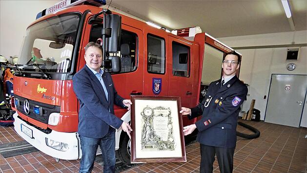 Durch Zufall ist Michael Krasser (links) auf eine 100 Jahre alte Urkunde gesto&szlig;en. Eigentlich wollte er sie am Festwochenende der Feuerwehr und des SV Fortuna &uuml;bergeben, doch das f&auml;llt aufgrund der Corona-Pandemie aus. Auch ohne gro&szlig;es Publikum freute sich Kommandant Markus Stumpf sehr.