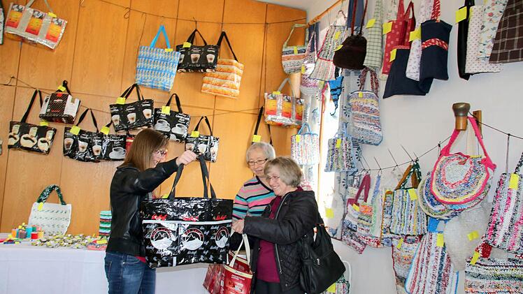 Bettina Eberhardt (links) freut sich über die gerade erstandene originelle Plastiktasche aus zusammengenähten ehemaligen Kaffeetüten. Wie ihre Mutter Hildegard (rechts) trägt die junge Frau aus Gleismuthhausen immer eine Einkaufstasche bei sich, um in Läden nicht auf Kunststofftragetaschen angewiesen zu sein. Christine Weschenfelder (hinten) und ihre Mitstreiterinnen von der Gemünner Lichtstube haben die Taschen angefertigt. Foto: Bettina Knauth