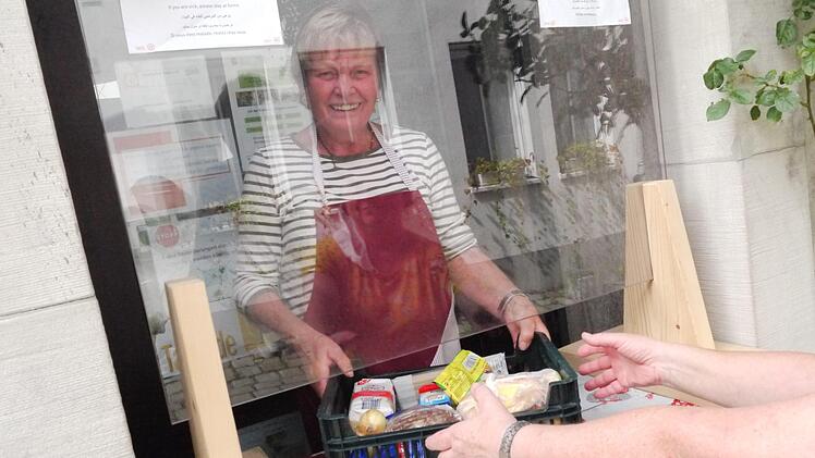 Tafel-Helferin Magda Weisensee demonstriert die Lebensmittel-Ausgabe in Corona-Zeiten. Stellwände mit durchsichtigen Scheiben schützen Helfer und Abholer.