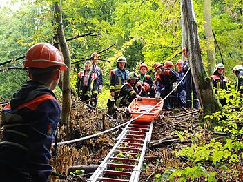 Mit Unterst&uuml;tzung durch erfahrene Feuerwehrleute mussten die Jugendlichen einen verletzten Waldarbeiter mit Hilfe einer Schleifkorbtrage aus unwegsamem Gel&auml;nde retten.  Foto: Luca Berger