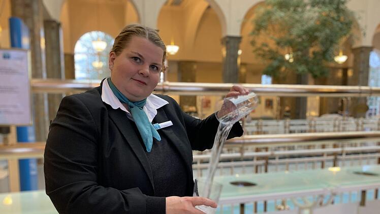 Brunnenfrau Lisa Lausenmeyer schwenkt das Heilwasser von Glas zu Glas. Der Heilwasserausschank in der Brunnenhalle ist wieder geöffnet. Foto: Anja Vorndran