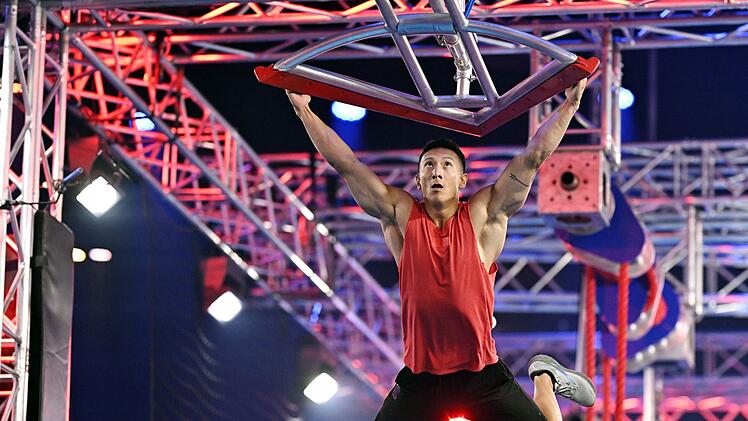 Dieses Hindernis, an dem sich hier David Wollschläger abmüht, heißt "Buschis Rache". Es ist ein Denkmal für Frank Buschmann, der seine letzte Staffel als Moderator von "Ninja Warrior Germany" (RTL) bestreitet. Zur Einweihung gibt's Schampus-Dusche. Buschi ist gerührt: "Das geht unter die Haut." Dann feixt er: "Da fliegt ihr alle rein, ihr Pflaumen."