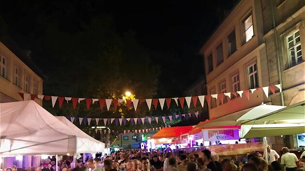 Nachtfest mit Menschenmenge bei der Bamberger Sandkerwa. Bunte Wimpelketten schmücken die Straße, beleuchtete Stände und Zelte sind zu sehen. Lebhafte Atmosphäre bei einer Feier.