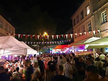 Nachtfest mit Menschenmenge bei der Bamberger Sandkerwa. Bunte Wimpelketten schmücken die Straße, beleuchtete Stände und Zelte sind zu sehen. Lebhafte Atmosphäre bei einer Feier.