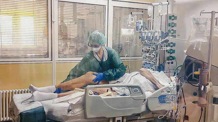 Eine Krankenpflegerin bettet auf der isolierten Covid-Station einen Patienten um. Die k&ouml;rperlich schwere Arbeitet verrichtet sie im wasserabweisender Schutzkleidung. Stundenlang.