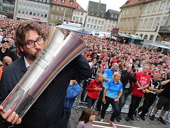 Brose Baskets-Coach Andrea Trinchieri posiert auf dem Maxplatz in Bamberg mit dem Pokal. Foto: Daniel Karmann/dpa