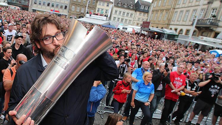 Brose Baskets-Coach Andrea Trinchieri posiert auf dem Maxplatz in Bamberg mit dem Pokal. Foto: Daniel Karmann/dpa