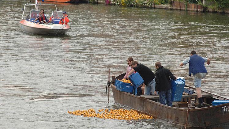 Menschen auf einem Boot setzen Plastikenten in einen Fluss. Eine andere Gruppe fährt in einem Motorboot. Das Bild ist bei der Bamberger Sandkerwa aufgenommen worden.