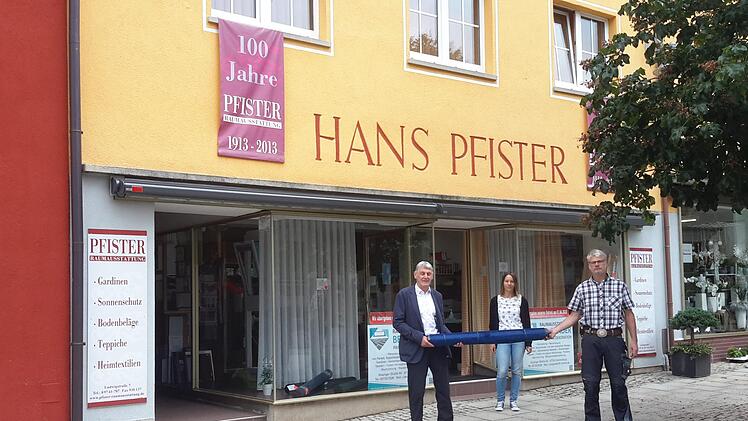 Mit einer Stoffrolle übergab Jürgen Pfister (links) seinen Geschäftsbetrieb an Jürgen Bergander (rechts). Ansprechpartnerin vor Ort ist weiterhin Martina Arnold (Mitte).  Foto:  Rolf Pralle
