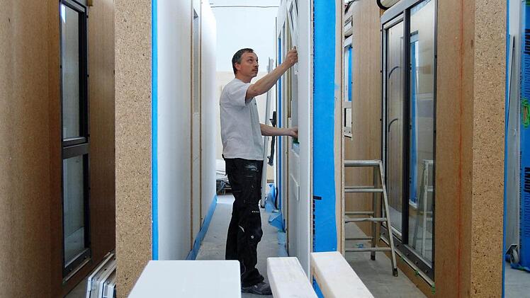 Ein Glaser setzt Fenster in eine Fertighaus-Wand ein