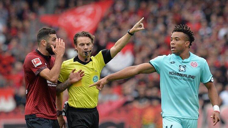 Schiedsrichter Guido Winkmann (Mitte) gestikuliert neben dem N&uuml;rnberger Mikael Ishak (li.) und dem Mainzer Pierre Kunde Malong. Der Aufsteiger und die Rheinland-Pf&auml;lzer trennten sich am Samstag 1:1.  Fotos: Timm Schamberger/dpa