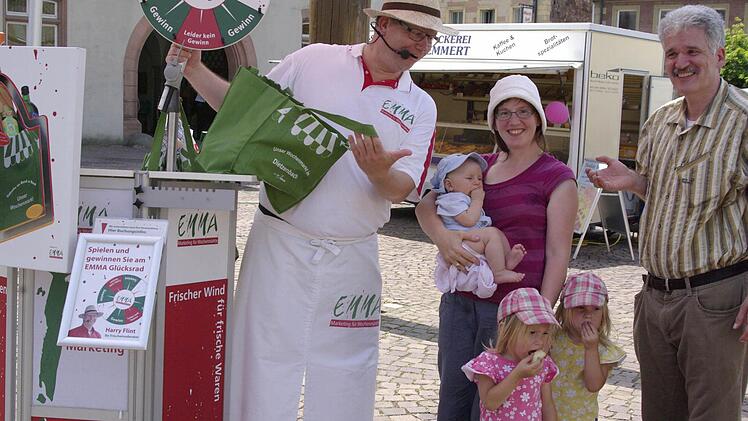 Marktmoderator Harry Flint (links) und der Prokurist der Deutschen Marktgilde, Uwe Lorey (rechts), überreichen am Samstag in Hammelburg eine Tasche mit frischem Obst und Gemüse an Gewinnerin Doris Aulig (Mitte) und ihre Kinder Matthäus, Sophia und Viktoria. Foto: Winfried Ehling