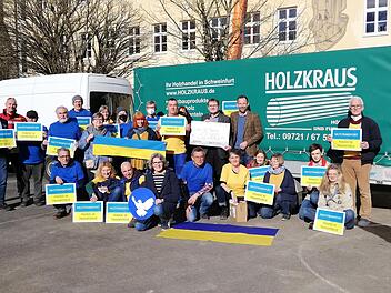 Der Präsident des Bad Kissinger Rotary-Clubs Philipp Cramer und Schatzmeister Werner Klöffel (mit Scheck) überreichten den symbolischen Scheck an die Münnerstädter Ukrainehilfe. Spontan waren Helfer in den Ukraine-Farben zur Übergabe gekommen. Foto: Heike Beudert