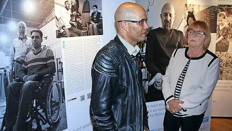Till Mayer vor Bildern seiner Ausstellung "Barriere: Zonen" im Gespräch mit der Dritten Bürgermeisterin der Stadt Zeil, Christl Pottler (ÜZL). Sie hält es mit Blick auf die Reportagen und Fotos des Bamberger Journalisten für wichtig, dass behinderte Menschen heute nicht mehr versteckt werden, wie es vor Jahren geschah. Und Christl Pottler weiß, wovon sie spricht, denn sie war 40 Jahre in der Pflege tätig. Auf der linken Ausstellungstafel ist der querschnittsgelähmte Osama aus Syrien zu sehen,...