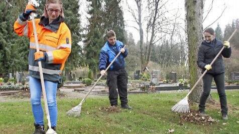Petra Barthelmes (von links), Susanne Hofmann und Simona Tutuianu kehren das Laub auf dem Friedhof an der Heimgartenstraße zusammen.  Foto: Andreas Schmitt