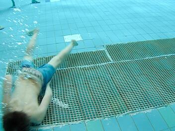 Ein Junge taucht über eine zweieinhalb Quadratmeter große Stelle im Freizeitbecken. Dort haben Stadtwerke-Mitarbeiter abgelöste Fliesen wieder mit Spezialkleber befestigt. Darüber wurde zusätzlich ein Gumminetz gespannt, damit sich keiner an Kanten verletzt. Foto: Ronald Rinklef