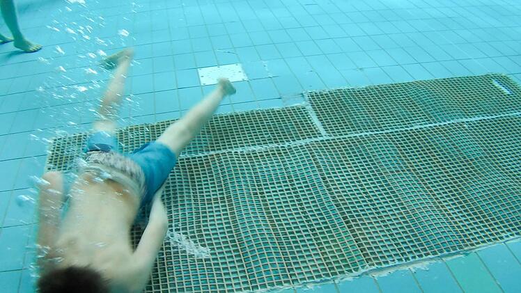 Ein Junge taucht über eine zweieinhalb Quadratmeter große Stelle im Freizeitbecken. Dort haben Stadtwerke-Mitarbeiter abgelöste Fliesen wieder mit Spezialkleber befestigt. Darüber wurde zusätzlich ein Gumminetz gespannt, damit sich keiner an Kanten verletzt. Foto: Ronald Rinklef