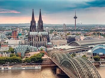 K&ouml;ln Luftaufnahme mit Z&uuml;gen, die auf einer Br&uuml;cke &uuml;ber den Rhein fahren, auf dem Frachtschiffe und Passagierschiffe verkehren. Im Hintergrund der majest&auml;tische K&ouml;lner Dom.  Cologne Aerial view with trains move on a bridge over the Rhine River on which cargo barges and passenger ships ply. Majestic Cologne Cathedral in the background