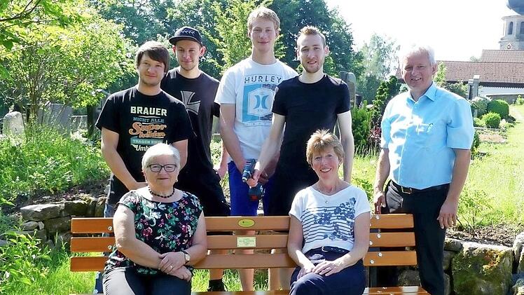 Probesitzen auf der neuen Bank im Friedhof: (vorne, von rechts) Christine Diersch, Brigitte Schröder, dahinter (von rechts) Bürgermeister Werner Diersch und die Vertreter der Strohberta, Christian Kauper, Patrick Munzert, Markus Schoberth und Patrick Hopfer. Foto: Dieter Hübner