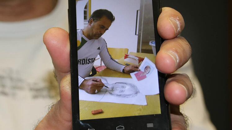 Auf seinem Handy hat er Fotos vom Entstehungsprozess der Zeichnungen. Hier überträgt er das Portrait von Bundeskanzlerin Angela Merkel auf Papier.