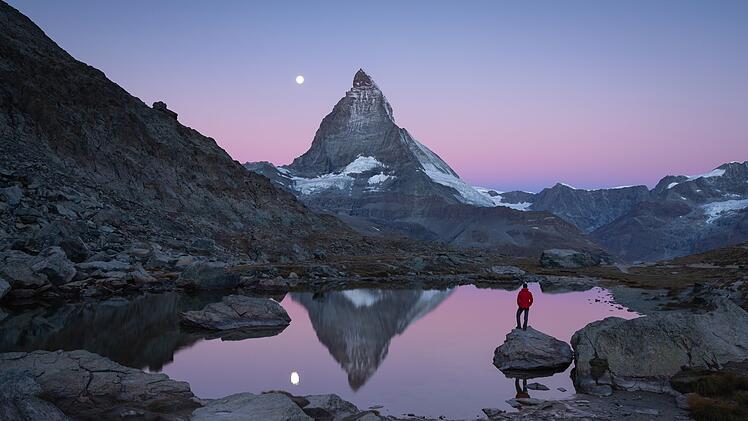 Hiker on a rock in the Riffelsee  at dawn, enjoying the Matterhorn view.