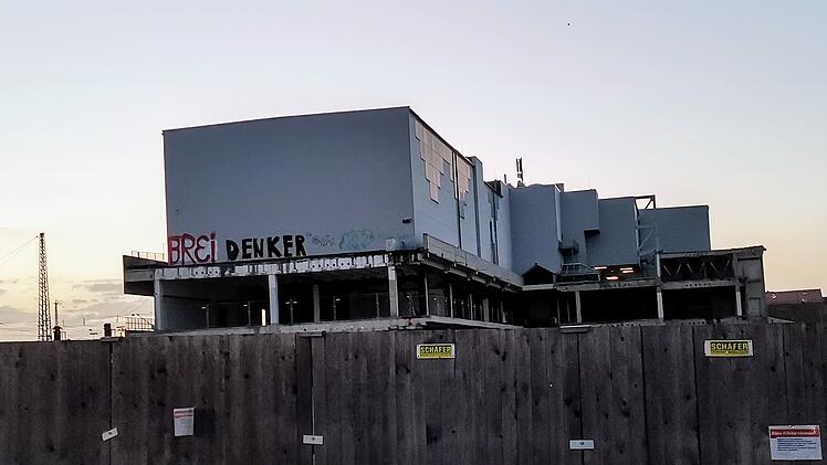 Ein teilweise erbautes Gebäude hinter einem Holzzaun. Graffiti auf der Fassade. Baustelle am frühen Abend.
