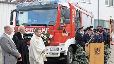 Die Zeiler Feuerwehr mit Kommandant Tobias Hetterich (Rednerpult) war vor dem neuen Auto angetreten, als es übergeben wurde. Mit im Bild, von links: der Zeiler Bürgermeister Thomas Stadelmann, der frühere Gemeindereferent Helmut Leykauf und Pfarrer Michael Erhart.  Foto: ks