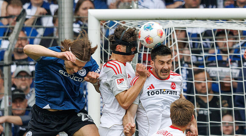 18.04.2026, Nordrhein-Westfalen, Bielefeld: Fu&szlig;ball, M&auml;nner: 2. Bundesliga, Arminia Bielefeld - 1. FC N&uuml;rnberg, 30. Spieltag, Sch&uuml;co Arena. Roberts Uldrikis (Arminia Bielefeld, l) im Kampf um den Ball mit Fabio Gruber (1. FC N&uuml;rnberg, M) und Luka Lochoshvili (1. FC N&uuml;rnberg, r) Foto: Friso Gentsch/dpa - WICHTIGER HINWEIS: Gem&auml;&szlig; den Vorgaben der DFL Deutsche Fu&szlig;ball Liga bzw. des DFB Deutscher Fu&szlig;ball-Bund ist es untersagt, in dem Stadion und/oder vom Spiel angefertigte Fotoaufnahmen in Form von Sequenzbildern und/oder video&auml;hnlichen Fotostrecken zu verwerten bzw. verwerten zu lassen. +++ dpa-Bildfunk +++
