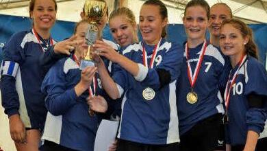 Da ist das Ding: Luisa Kaemmer (ganz links),    Alisia Hofmann (Dritte von rechts) und die anderen Spielerinnen der Bayern-Auswahl freuen sich, geschmückt mit ihren Goldmedaillen,  über den Pokal.  Nach dem Sieg hatte sich die ganze Bayernauswahl auf den nassen Rasen geworfen und war zu den applaudierenden Fans hingerutscht - wie beim Fußball. Foto: Faustball-Verband