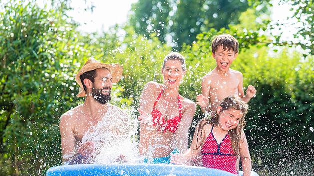 Family in garden pool splashing water cooling down, mother, father and kids having fun together Familie spitzt mit Wasser im Garten Swimming Pool bei Abkühlung, Mutter, Vater und Kinder in einem Becken