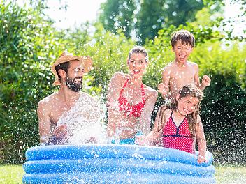 Family in garden pool splashing water cooling down, mother, father and kids having fun together Familie spitzt mit Wasser im Garten Swimming Pool bei Abkühlung, Mutter, Vater und Kinder in einem Becken