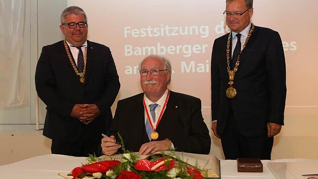 Nachdem er die B&uuml;rgermedaille in Empfang genommen hatte, trug sich der fr&uuml;here Regierungspr&auml;sident Wilhelm Wenning in das Goldene Buch der Stadt Bamberg ein. Rechts Oberb&uuml;rgermeister Andreas Starke, links B&uuml;rgermeister Wolfgang Metzner  Foto: Barbara Herbst
