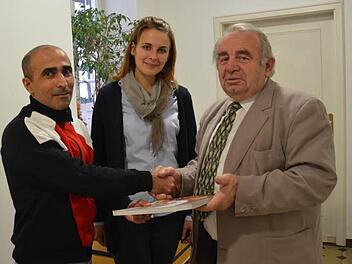 Asylbewerber Satullajew Sulejman (links) bedankt sich stellvertretend bei Heinz Hausmann (rechst) für die Hilfe, die er speziell in Kronach erfahren hat. Hausmann wiederum überreicht ein heimatkundliches Buch an den Journalisten. Mit im Bild: Julia Mari, die als Dolmetscherin fungierte.  Foto: K.-H. Hofmann