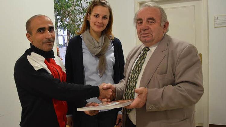 Asylbewerber Satullajew Sulejman (links) bedankt sich stellvertretend bei Heinz Hausmann (rechst) für die Hilfe, die er speziell in Kronach erfahren hat. Hausmann wiederum überreicht ein heimatkundliches Buch an den Journalisten. Mit im Bild: Julia Mari, die als Dolmetscherin fungierte.  Foto: K.-H. Hofmann