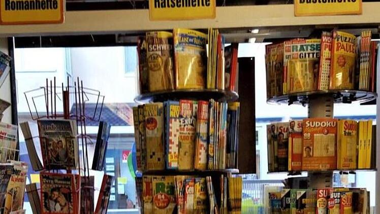 In einem Schreibwarengeschäft stehen Regale mit Roman-, Rätsel- und Bastelheften. Außen sieht man ein Schaufenster.