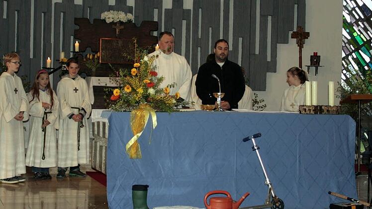 Die Angelausrüstung (rechts am Altar) und die Symbole der Fürbitten, die in der Kirche gesammelt wurden, finden sich vor dem Altar beim Familiengottesdienst in der Pfarrei Heilig-Geist in Ludwigsstadt; hinter dem Altar steht Pastoralreferent Grünbeck mit den Ministranten. Foto: Büttner