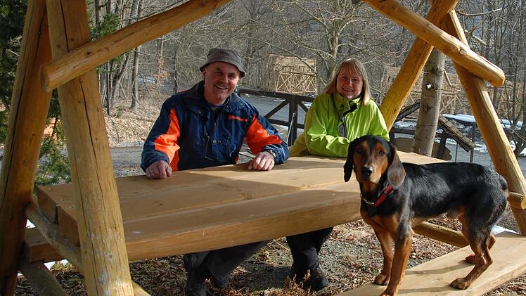 Gemütliche Sitzgruppen aus heimischem Holz laden die Besucher des runderneuerten Naturlehrpfads zum Verweilen ein. Stadtförsterin Carmen Hombach mit ihrem Jagdhund Toni und Forstwirt Georg Schaller sind mit der selbstgefertigten Konstruktion sehr zufrieden. Foto: Dagmar Besand