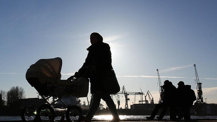 Eine junge Frau mit Kinderwagen geht am 08.02.2015 im Gegenlicht der Sonne. Foto: Bodo Marks/dpa