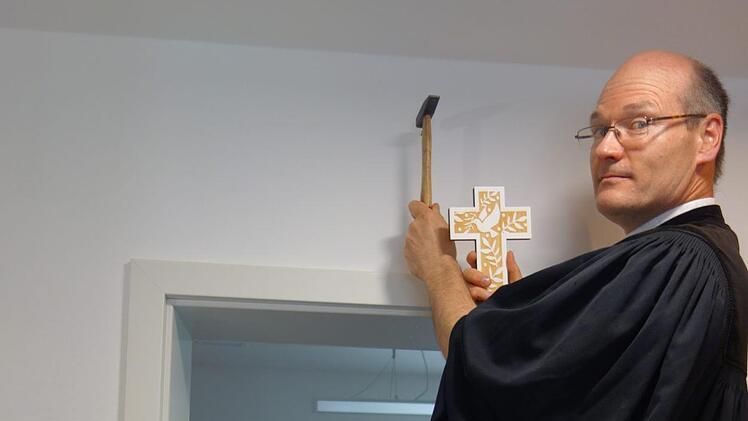 Höchst persönlich nagelt Pfarrer Andreas Neeb das Gastgeschenk, ein Kreuz, zur Freude von Silvia Schinkel an die Wand. Foto: Doris Weidner