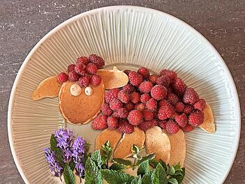 Süßes Schaf aus Pfannkuchen und Himbeeren auf Kräuterblumenwiese.