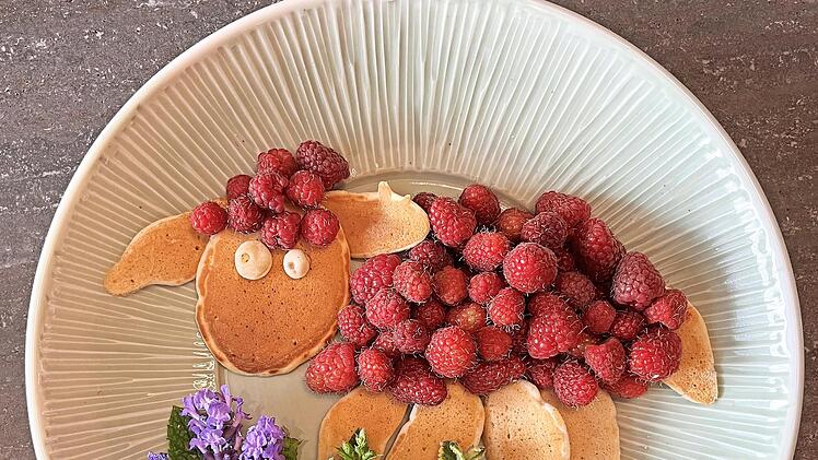 Süßes Schaf aus Pfannkuchen und Himbeeren auf Kräuterblumenwiese.