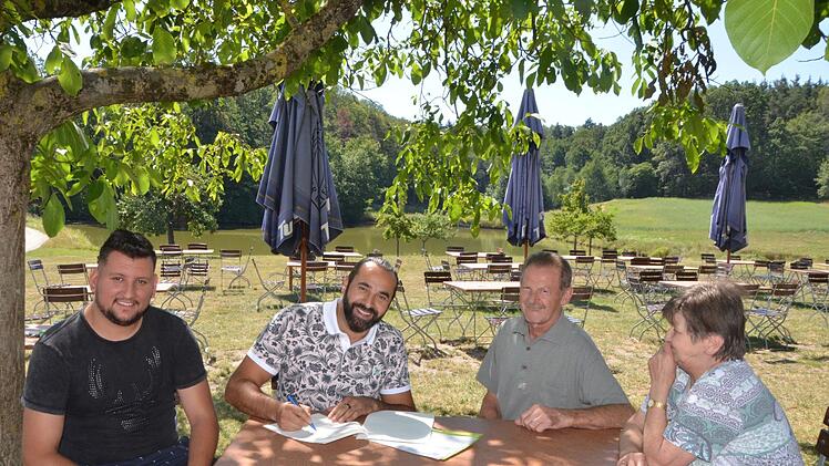 Sami Alijaj unterzeichnet im idyllischen Biergarten den Vertrag. Gemeinsam mit seinem Mitarbeiter Alex Vladulescu (links) hat er das Gasthaus Gumbrecht in Obermembach gepachtet. Hans und Elfriede Gumbrecht freuen sich auf die Nachfolge.  Foto: Bernhard Panzer