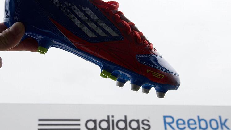 Ein Adidas-Schuh wird am 03.07.2013 in Rieste (Niedersachsen) vor das Logo von Adidas und Reebok gehalten. Foto: Friso Gentsch/dpa