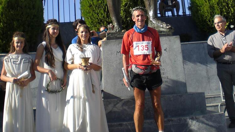 Ziel des Spartathlons ist keine Linie. Für die Teilnehmer ist der Lauf dann abgeschlossen, wenn sie den Fuß der Statue des legendären Königs der Spartaner, Leonidas, berühren. Davor steht Hubert Karl mit Lorbeerkranz und Urkunde, daneben die Ehren-Delegation der Stadt Sparta im historischen Gewand.