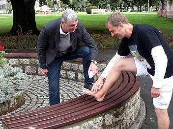 Assistiert vom 2. Bürgermeister Jürgen Pfister (links) trifft Barfußläufer Frank Jester vor dem Badhotel die Vorbereitungen für die nächste Etappe. Ein kühlendes Bad Brückenauer Pflegegel ist da eine willkommene Erfrischung.Foto: Rolf Pralle