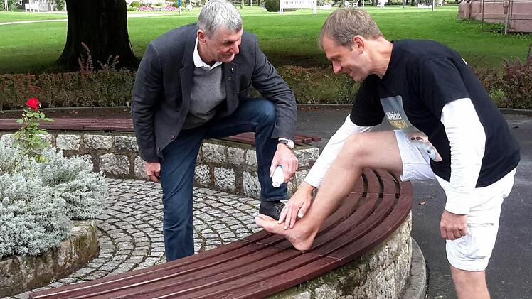 Assistiert vom 2. Bürgermeister Jürgen Pfister (links) trifft Barfußläufer Frank Jester vor dem Badhotel die Vorbereitungen für die nächste Etappe. Ein kühlendes Bad Brückenauer Pflegegel ist da eine willkommene Erfrischung.Foto: Rolf Pralle