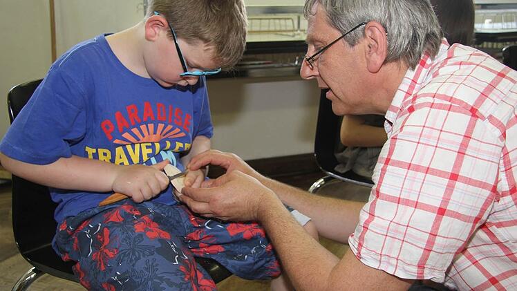 Emil lässt sich von Roland Friedrich die Tricks zeigen. Mit dem Handschnitzmesser schnitzt man immer Richtung Daumen, niemals von sich weg, das wäre zu gefährlich. Fotos: Sonja Adam