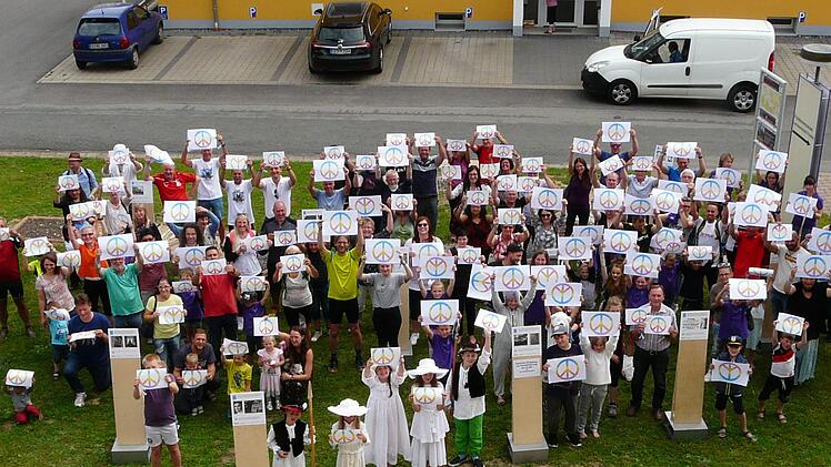 Schulkindern und Erwachsene halten das Peace-Zeichen hoch. Foto: Karin G&uuml;nther